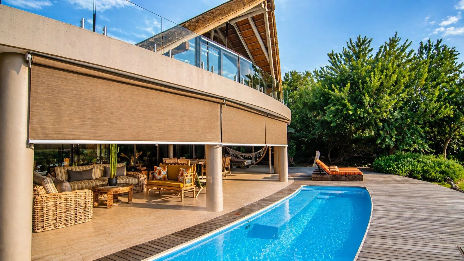 Curved poolside terrace with a covered lounge and the lodge’s thatched roofline